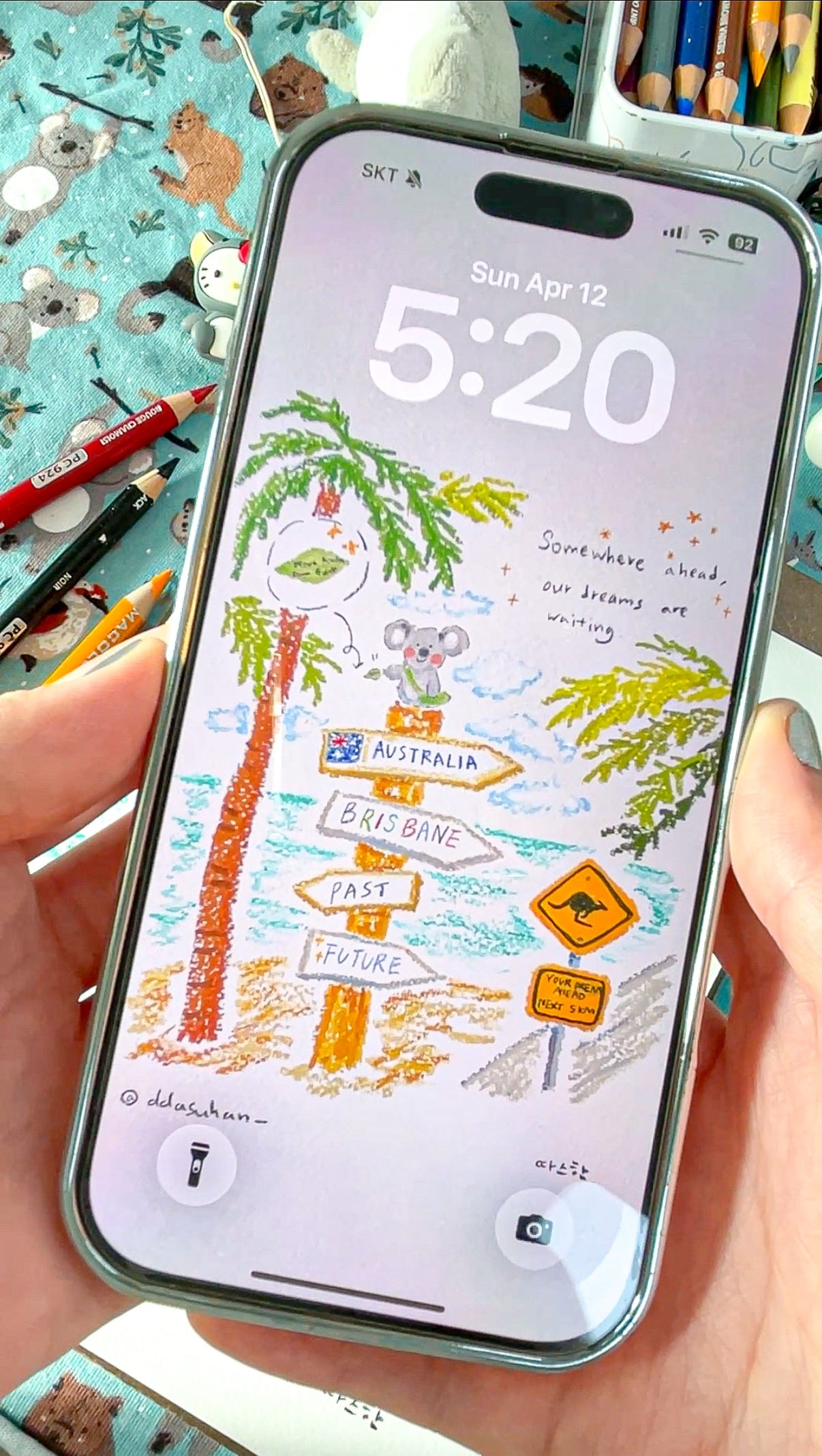 Phone with a travel-themed screen held by a hand, surrounded by stationery items.